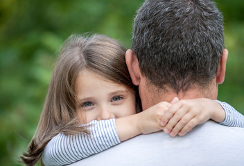 Fototapeta premium Portrait of cute little girl held in father's arms. Happy loving family. Father and his daughter child girl playing hugging. Cute baby and daddy. Concept of Father day. Family holiday and togetherness