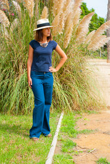 Young beautiful woman in boho style clothes with hat, jeans and necklace in park. Casual style model.