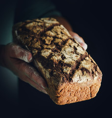 Female hands hold dark rye bread. Baker with fresh bread on a dark background.