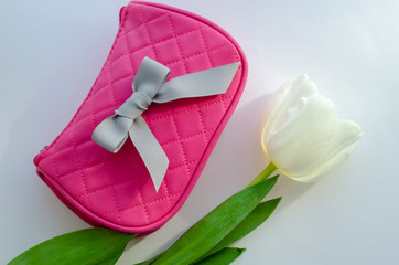white tulip flower. pink cosmetic bag, makeup brushes, cosmetics on white background