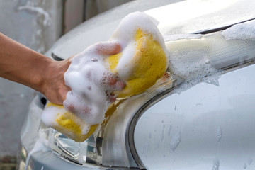 a hand using the soapy yellow sponge to wash the car