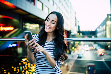 Cute lovely young woman using smart phone on evening city background