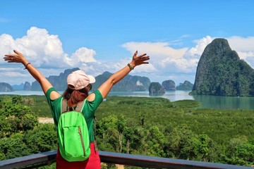 Back side of Woman traveler with small backpack & hat enjoying ocean view with mangrove forest, mountains & white clouds blue sky at SaMet NangShe viewpoint. Tropical summer holiday vacation concept