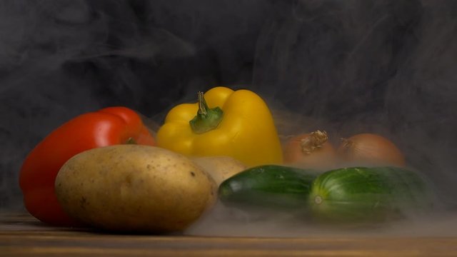 Fresh vegetables Bulgarian pepper, cucumbers, potatoes and onions on a black background from the vegetables blows cool and fresh, close-up, slow motion