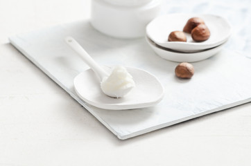 Shea butter in ceramic spoon on white background with nuts and moisturizer creme. Free text space.