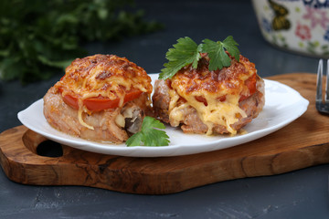 Chicken thighs with tomatoes and cheese arranged in a plate on a wooden board