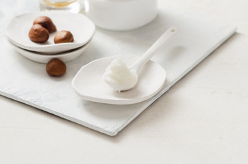 Fototapeta na wymiar Shea butter in ceramic spoon on white background with nuts and moisturizer creme. Free text space.