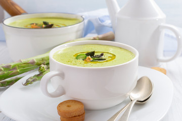 Asparagus cream soup in a white bowl with olive oil .