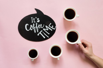 Creative flat lay top view. Woman's hand holds a cup of coffee up on pastel millennial pink paper background copy space.