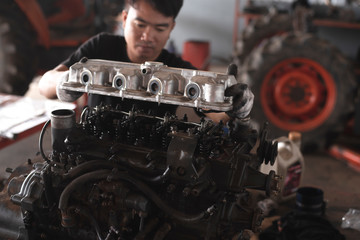The car mechanic is working with the car engine in the garage, repairing the tractor for agriculture.