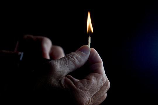 Burning match in old grandmother's hand close up