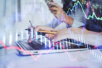 Hands typing on laptop. Business and Financial concept. Double exposure of stock market charts.