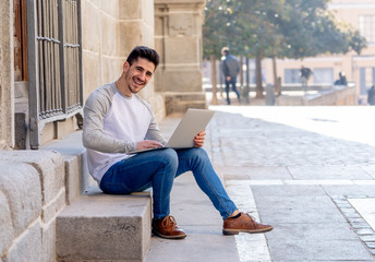 Young handsome man working and studying on laptop in a european city outdoors