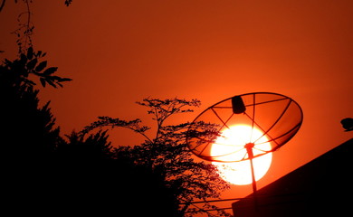 Red hot sun sets behind a satellite dish in Bangkok, Thailand