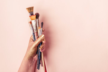 Artist golden hand with set of brushes on pale pink background