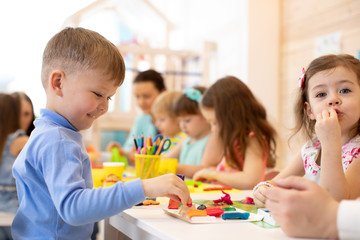 kid boy playing with colorful clay with group of children in kindergarten