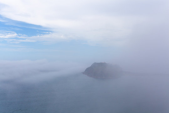 Low clouds and mist over ocean concealing a small island - mystical landscape