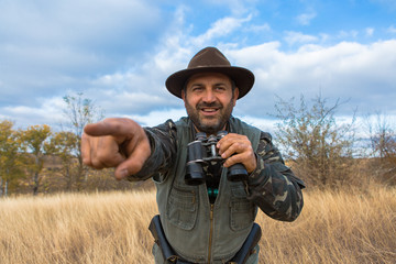 A hunter in a hat with binoculars looks out for prey	