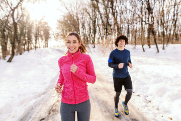 Happy Caucasian friends in sportswear running outdoors. Wintertime, snow all around. Healthy lifestyle concept.