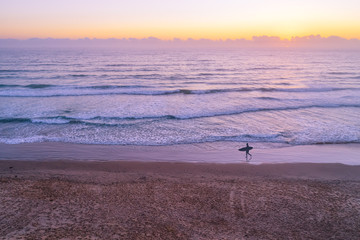 Fototapeta na wymiar Surfer silhouette walking on ocean beach at dawn with copy space