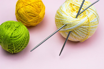 Products for needlework, knitting. Balls of yellow, green, purple yarn, knitting needles on a pink background. Space for text.