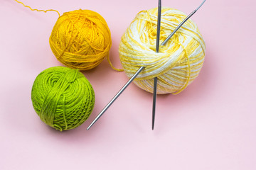 Products for needlework, knitting. Balls of yellow, green, purple yarn, knitting needles on a pink...