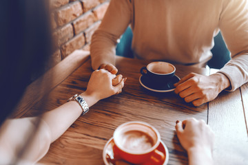 Caucasian Couple in love sitting in cafeteria, drinking coffee and holding hands. Cropped image.