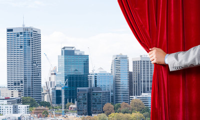 Modern business cityscape behind curtain opened by businessman hand