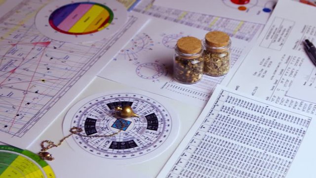 Pendulum for tarot and astrological circle on the background of astrological charts, magical potions and astrological spreadsheets