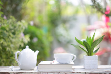 White coffee cup and kettle with notebook on wooden table with green plants