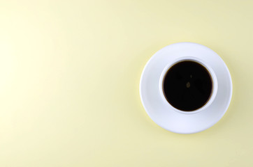 One cup with a saucer with coffee on a light yellow background.
