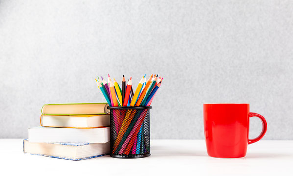 colorful pencils, books and red cup on a desk with gray background