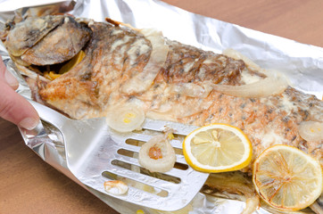 Closeup of spatula,slices of lemon on grilled carp fish burned to a crisp