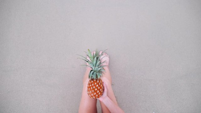 Top view of woman holding pineapple sexy legs on beach self shot.