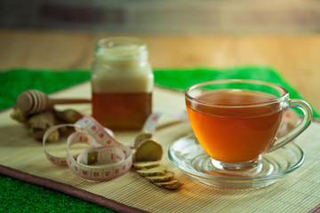 Ginger juice in a clear cup and honey jar placed beside with measuring tape..Concept of healthy.