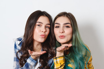 Fototapeta premium Two attractive young woman with shiny makeup sending air kiss, looking at camera, on white background
