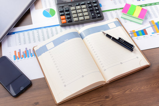 Open leather notebook, drawings, charts, phone, calculator, pencil and laptop on the desk in the office. Business and Finance.