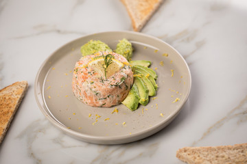 Rohes Lachstatar mit Lachs, Dill, Zitrone, Avocado und Vollkorn Toast Brot auf Porzellan Teller und...