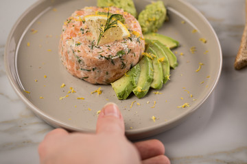 Frau isst rohes Lachstatar mit Lachs, Dill, Zitrone, Avocado und Vollkorn Toast Brot auf Porzellan...