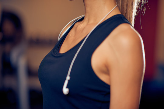Close up of woman's breasts in sport top. Around neck earphones. Gym interior, healthy lifestyle concept.