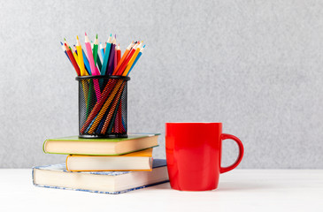 books, colorful pencils and red cup on a desk with gray background