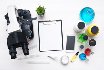 Laboratory table with a blank paper sheet of researching results, microscope, mobile phone and a chemical reagent liquids background with copy space. Medical analysis. Flat lay.