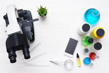 Laboratory table with a microscope, mobile phone and a chemical reagent liquids above. Chemistry or pharmacy background with copy space. Flat lay.