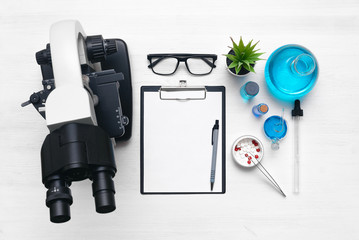 Laboratory table with a blank paper sheet of researching results, microscope and a chemical reagent...