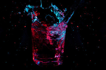Liquid splashing from rocks glass with many droplets glowing in red and blue on a black background