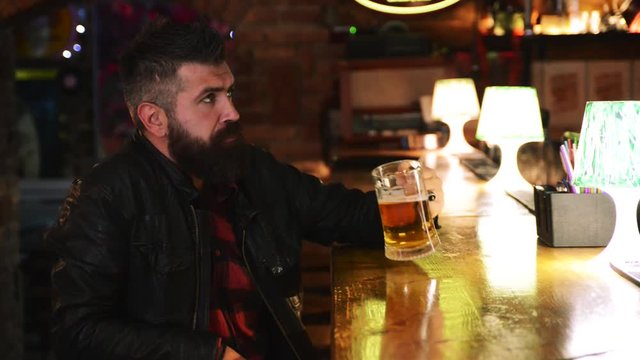 Bearded brutal man drinking beer at the bar counter. Handsome male fan watching sport game at the pub.