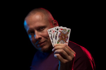 A man holds a deck of cards and shows tricks in a scenic light.