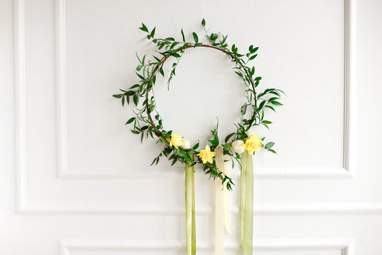 Beautiful hand made everlasting dry wreath made of nartsyss, colourful feathers and eucalyptus on the white wall background