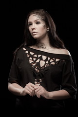 portrait of young brunette girl with black tears from eyes and lace pattern on face and neck posing...