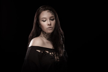 portrait of young brunette girl with black tears from eyes and lace pattern on face and neck posing...
